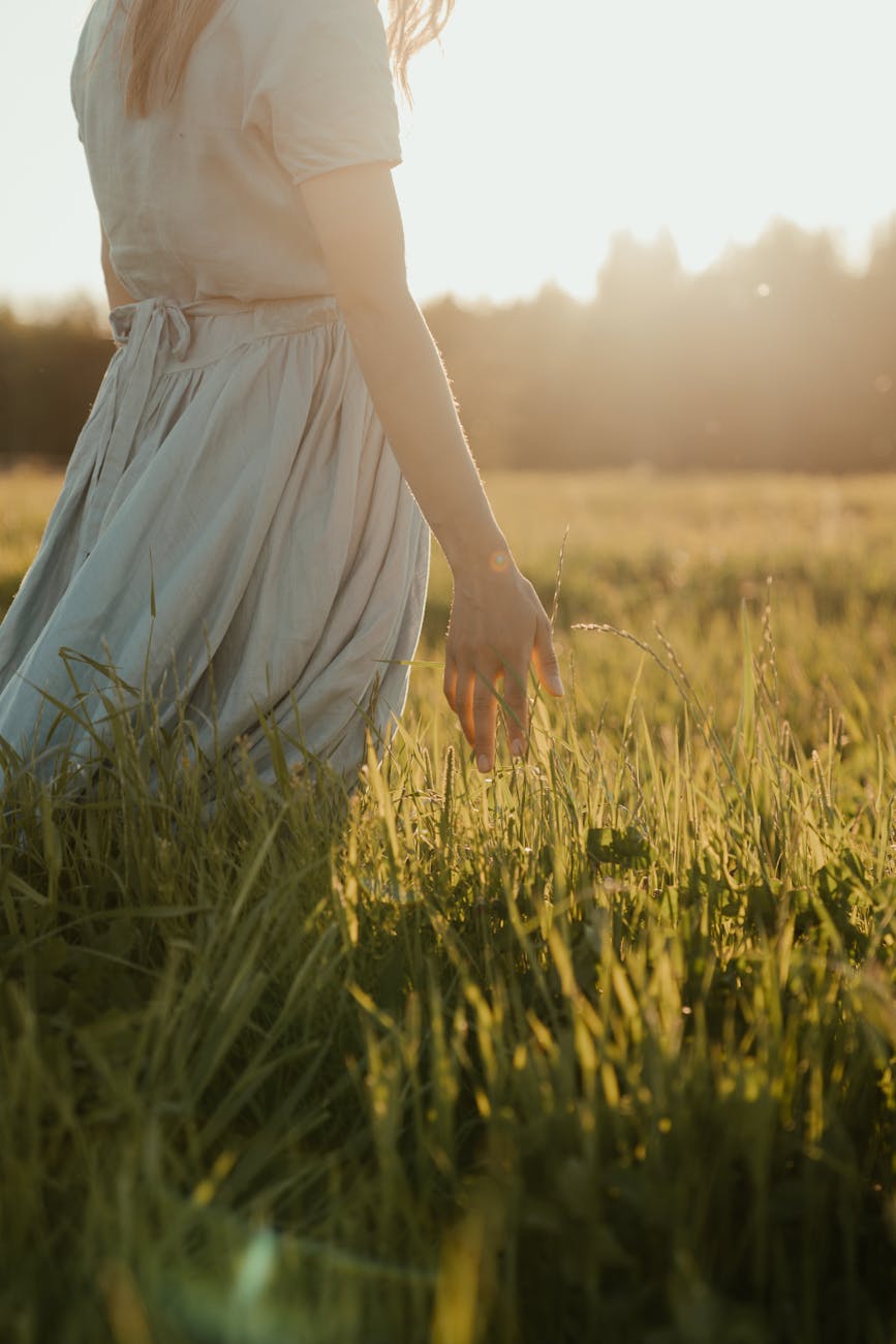 Woman standing in a sunlit meadow with eyes closed and gentle smile, embodying a pet caregiver in the quiet, ongoing stages of grief beginning to feel quietly proud of the love she gave.